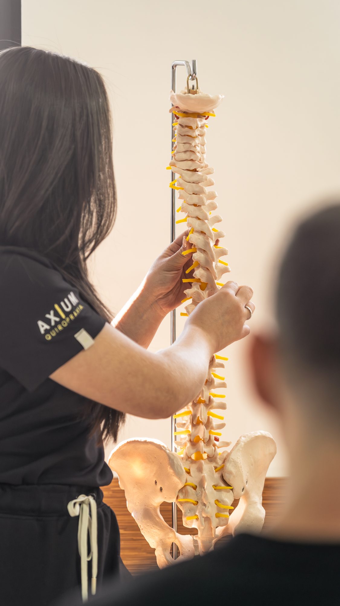 Quiropraxista da Axium realizando ajuste lombar, com modelo anatômico de coluna ao fundo
